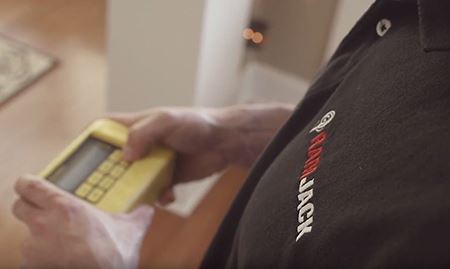 A shallow depth of field focused on a Ram Jack technicains shirt logo looking down at a device in their hands used to inspect a property foundation